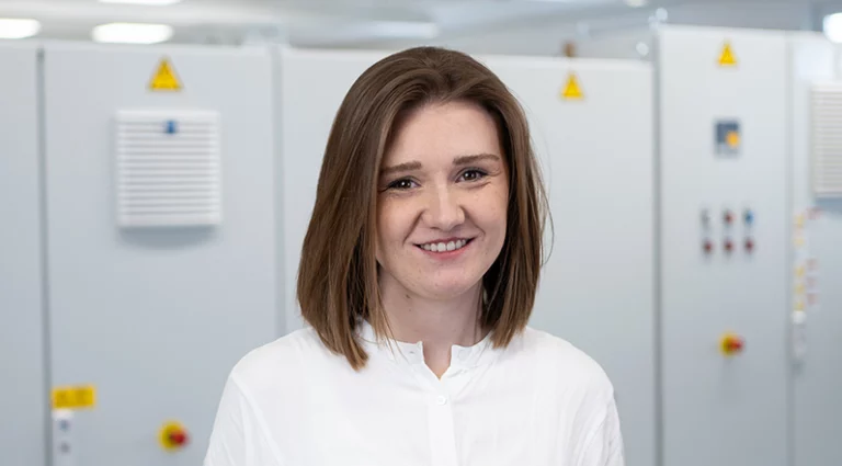 A woman in a white shirt stands in front of control systems at Krayer Systemtechnik.