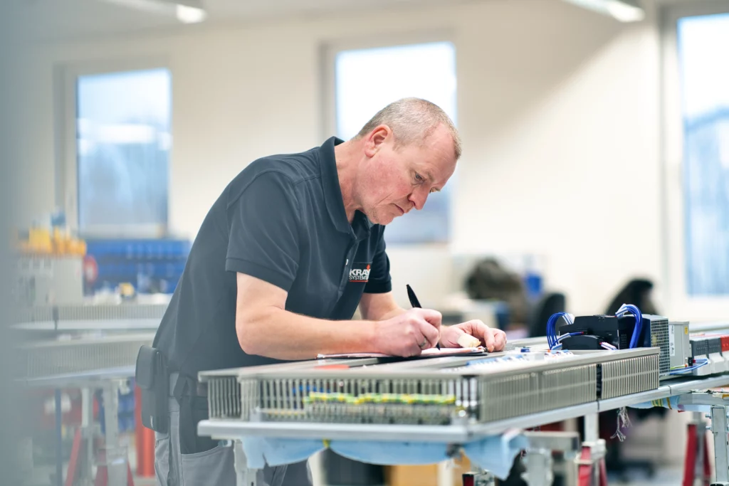 Mitarbeiter dokumentiert und prüft Arbeitsschritte während der industriellen Montage von Schaltschränken.